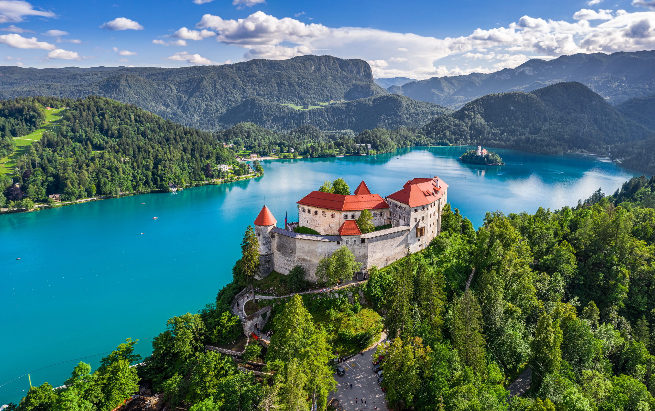 Aerial panoramic view of beautiful castle with lake, the church and alps at background on a bright summer day